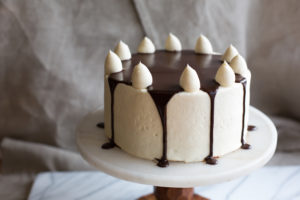 The Mad Hatter's Black and White Cake iced in vanilla buttercream, with dollops of vanilla buttercream and poured chocolate ganache.