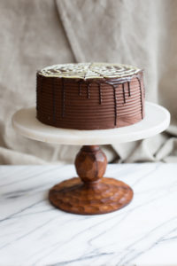 The Mad Hatter's Boston Cream Cake with dark chocolate fudge icing, and poured chocolate ganache on a serving dish.