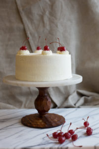 The Mad Hatter's Black Forest Cake, coated in whip cream, chocolate shavings, and cherries on a serving dish.