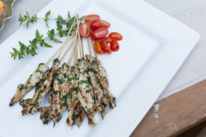 The Mad Hatter's Chicken Skewers with fresh tomatoes on a white serving dish.