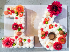 Number 16 custom birthday cake with fresh flowers, strawberries, raspberries, macarons, and whipped cream for special occasions.