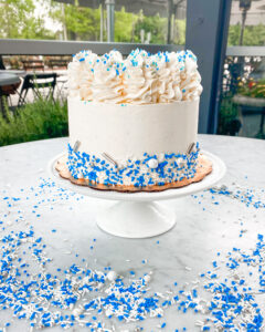 Graduation white and blue sprinkled celebration cake, ideal for brunch or breakfast gatherings, displayed at Mad Hatter Cafe & Bakeshop in Durham.