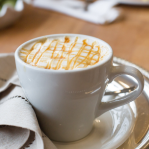 A cup of artisan coffee with caramel drizzle, elegantly served on a silver tray at Mad Hatter Cafe & Bakeshop in Durham