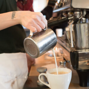 Barista at Mad Hatter Cafe Durham skillfully pouring milk to create latte art, showcasing coffee craftsmanship