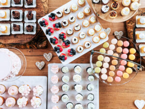 Elegant wedding dessert bar with assorted mini cupcakes, tarts, macarons, and decorated cookies.